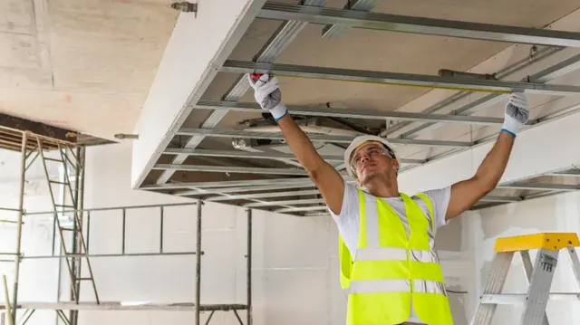 Plaquiste professionnel posant une plaque de plâtre sur un chantier de rénovation