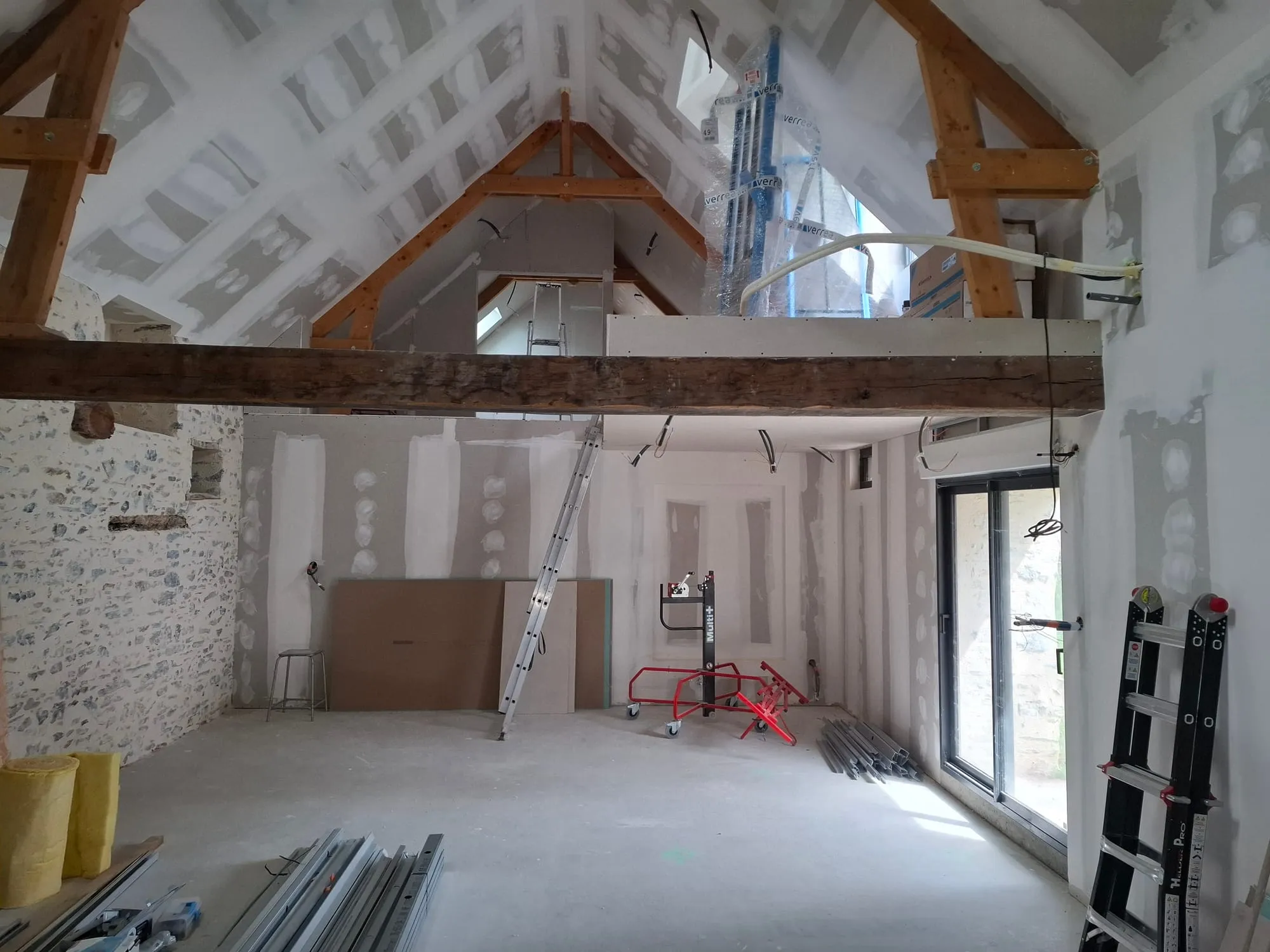 Grande pièce de vie sous charpente avec cloisons en placo, mezzanine, poutre ancienne et mur en pierre conservés