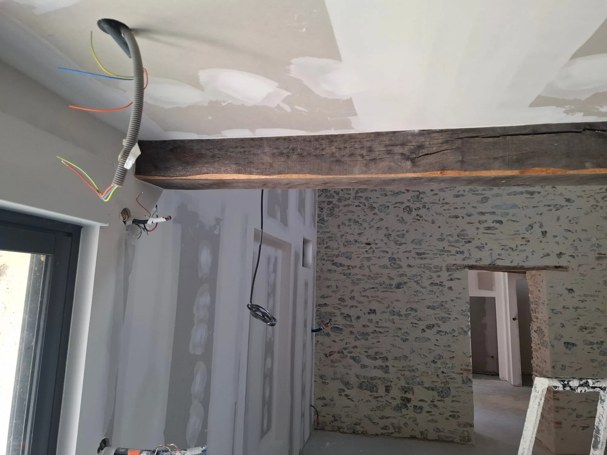 Séjour avec mur en pierre apparent conservé, poutre ancienne et cloisons neuves en placo